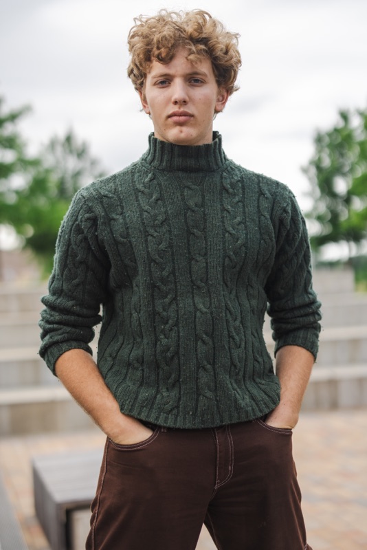 Young man in a green cable-knit turtleneck with his hands in his pockets