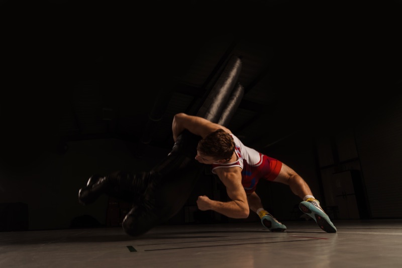 Wrestler diving low across the mat against a dark backdrop