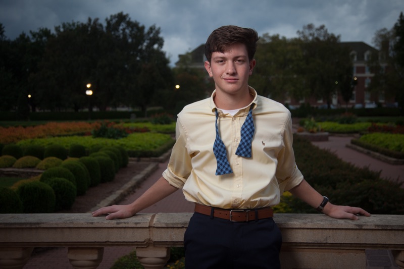 Young man in a pale yellow shirt with an untied bow tie at a garden balustrade at dusk
