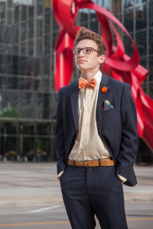 Young man in a navy suit and orange bow tie in front of a red downtown sculpture