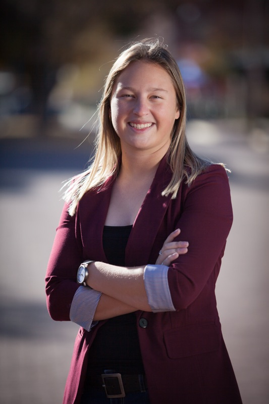 Smiling young woman in a burgundy blazer with her arms crossed